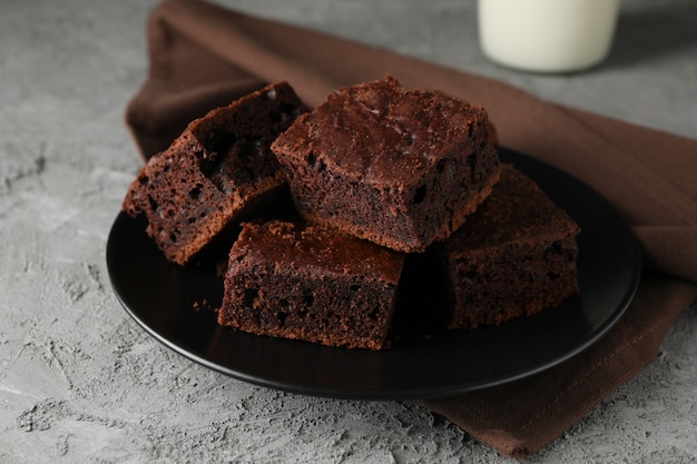 Platte mit Schokoladenkuchenscheiben und Flasche Milch auf grauem Tisch, Nahaufnahme