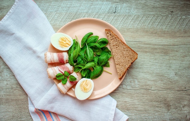 Platte mit Spinatblättern, grünem Basilikum, Speck, Eiern und einem Stück Roggenbrot Essen zum Frühstück