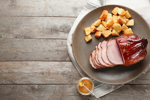 Platte mit traditionellem, in Scheiben geschnittenem, mit Honig gebackenem Schinken und Kartoffeln auf dem Tisch