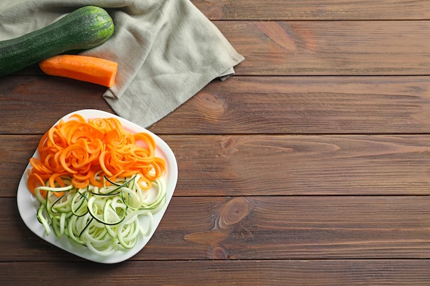 Platte mit Zucchini- und Karottenspaghetti auf Holzhintergrund