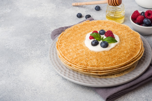 Platte von köstlichen dünnen Pfannkuchen mit Beeren auf grauer Tabelle