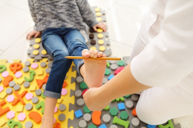 Plattfußbehandlung für Kinder mit speziellem Massageteppich. Kleines Mädchen auf Massagematte, das Übungen zur Vorbeugung von Plattfüßen macht. Fußstärkungsübungen. Podologie-Klinik.