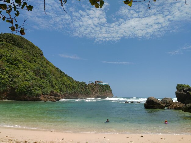 Foto una playa con un acantilado y una casa en el lado derecho.