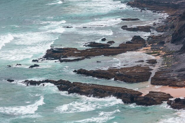 Playa de arena con crestas pedregosas tiempo nublado vista en verano costa rocosa del Atlántico (Costa Vicentina, Algarve, Portugal). Y olas del océano.