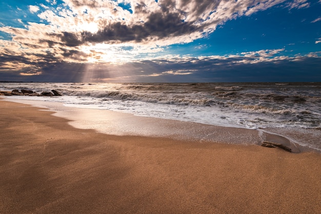 Una playa de arena dorada, pequeñas olas y un hermoso cielo dramático.