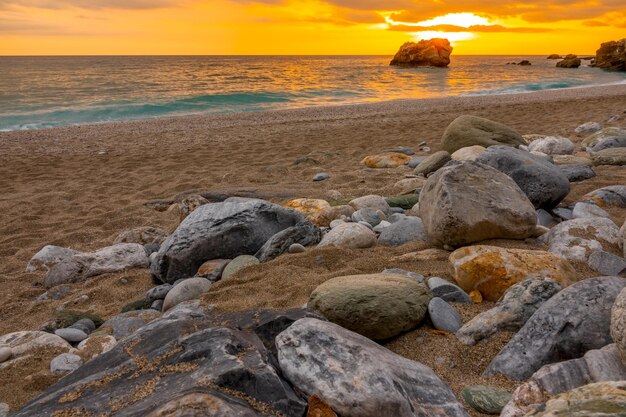 Playa de arena gruesa y piedras de colores. Puesta de sol dorada sobre el mar en calma