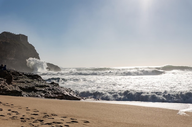 Playa de arena con huellas y olas rompiendo contra las rocas