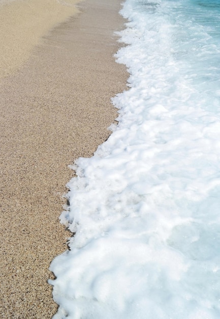 Playa de arena y mar de olas azules con espuma blanca.