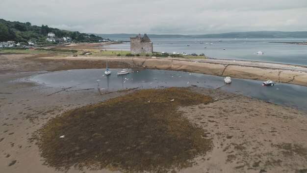 Playa de arena marrón de la bahía del mar pájaro volador aéreo en la orilla del océano ruinas del antiguo castillo histórico en la playa