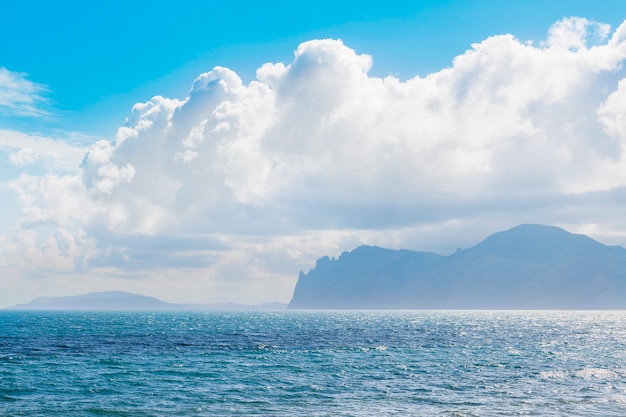 Playa de arena con montañas al fondo. Las montañas están cubiertas de hierba y tienen escarpados acantilados desde el mar. El cielo esta nublado