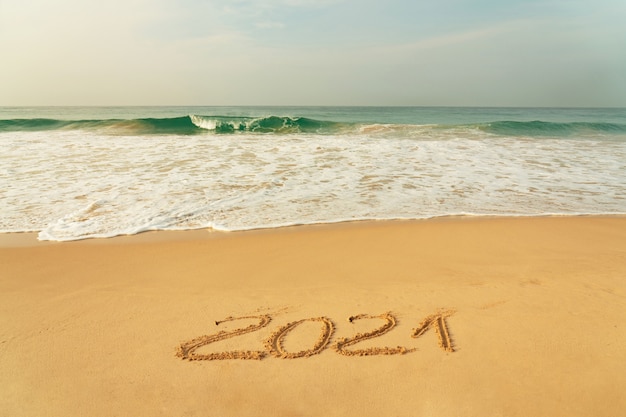 Playa de arena con el símbolo del Año Nuevo 2021 y olas azules, Sri Lanka.