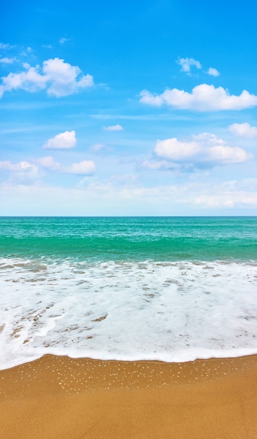 Playa de arena con suave oleaje y cielo azul con nubes blancas - fondo vertical con espacio para su propio texto