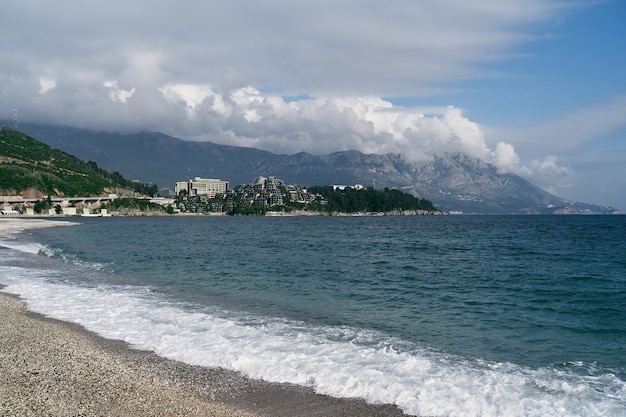 Playa en budva con vistas al mar, montañas y edificios.