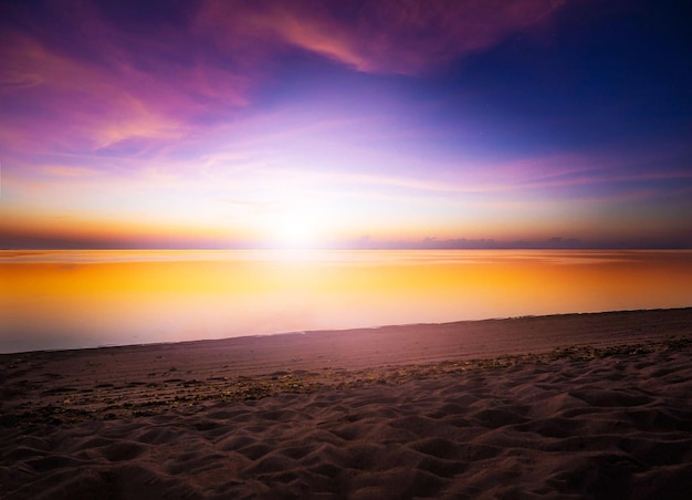 Una playa con un cielo morado y naranja y el sol se está poniendo