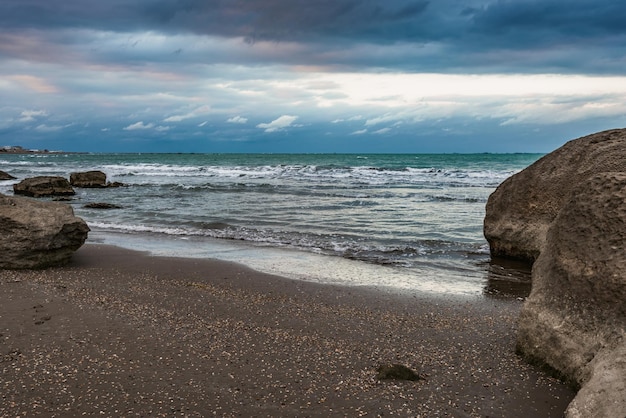 Una playa con un cielo nublado y una gran roca en la orilla.