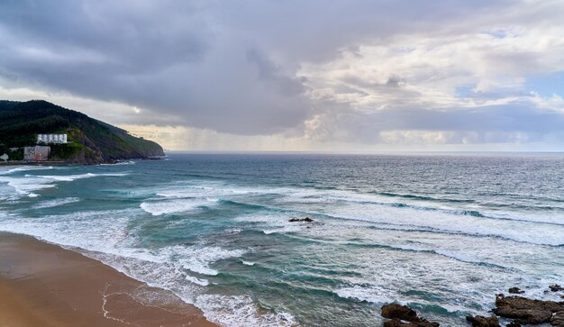 Foto playa en la costa en un día nublado con fondo tormentoso con lluvia sobre la vista alta del mar