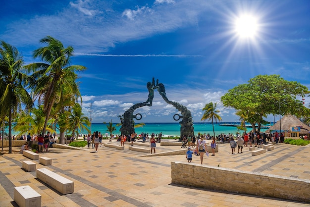 PLAYA DEL CARMEN MEXIKO APR 2022 Besucher vermischen sich am Strand des Fundadores Park in Playa del Carmen an der karibischen Küste der Riviera Maya mit Darstellern unter der Portal Maya-Skulptur