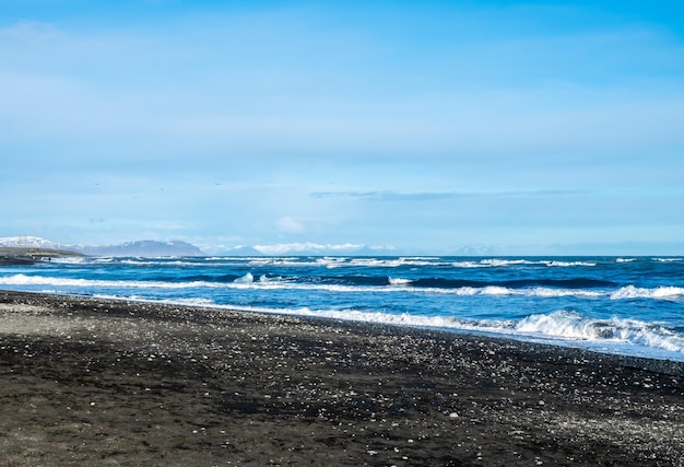 Playa de diamantes de arena negra con olas y montañas nevadas en Islandia