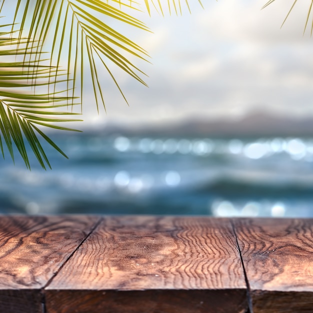 Playa con hoja de coco de palma y mesa de madera vieja en la playa borrosa y vista para promover el concepto de producto. Concepto de verano relajarse y fiesta.