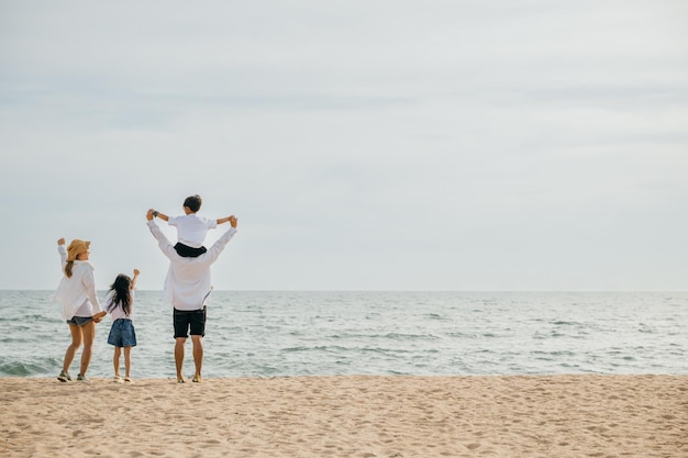 Foto en la playa de la mar una familia de cuatro personas experimenta la felicidad con los brazos levantados al atardecer el padre llevando a su hijo en los hombros captura los momentos despreocupados de unas memorables vacaciones de verano