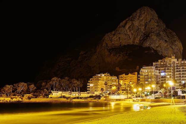 Playa de noche con edificios iluminados y una gran montaña al fondo junto al mar. Calpe Alicante.