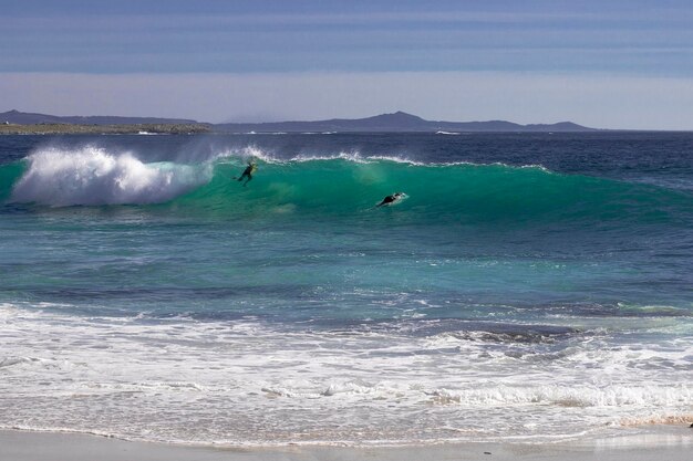 Playa con olas turquesas donde dos surfistas se están divirtiendo