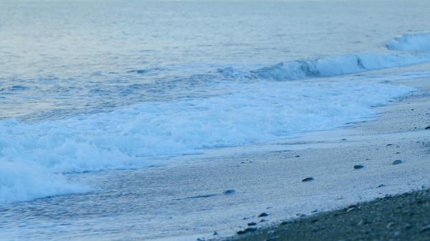 La playa de piedras de guijarros al atardecer las olas de agua espumosa que se estrellan en la playa de guiyarros al anochecer en tiempo real