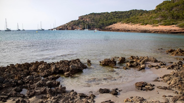 Una playa con rocas y botes en el agua.