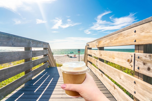 Playa de rocas indias en Florida, EE.UU. con la mano sosteniendo una taza de papel de café caliente