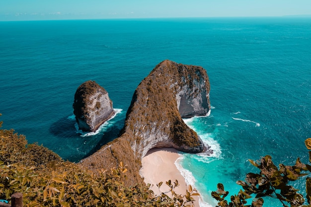 Una playa rocosa con una playa de arena rosa al fondo.