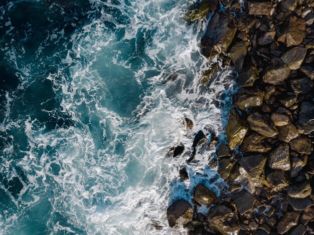 Foto playa rocosa en el sur de tenerife con olas que chocan contra la playa de piedras volcánicas