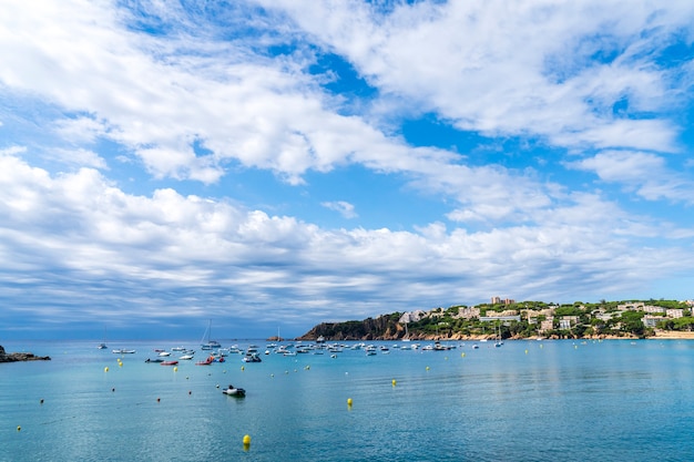 Playa de Sant Pol con barcos en el mar en un día con algunas nubes blancas.