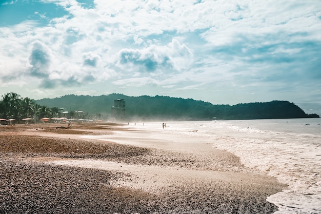 Playa con sillas y sombrillas con la selva y la montaña. Jaco, Costa Rica