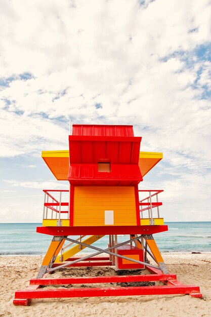 Foto playa del sur de miami. colorida casa de salvavidas o edificio de torre art deco salvavidas de color rojo y naranja en la playa de arena cerca del mar, agua del océano sobre fondo de cielo nublado, viajes y vacaciones