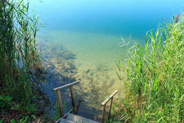 Playa tranquila del lago de verano con pendientes de madera hasta el agua