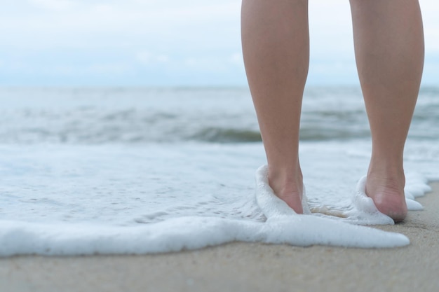 En una playa tropical de arena con un fondo de cielo azul, los pies de una mujer caminan lentamente y se relajan