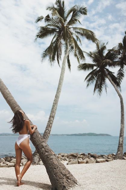 Foto playa tropical con palmeras y chica de moda de lujo en traje de baño blanco