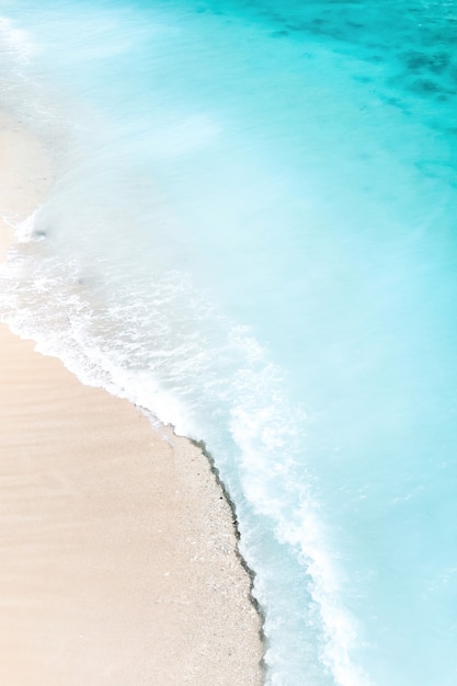 Playa tropical con vista de pájaro de las olas rompiendo en la playa tropical de arena dorada. Las olas del mar dan vueltas suavemente a lo largo de la hermosa playa de arena.