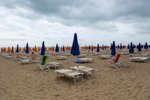 Playa vacía en otoño en Italia, sombrillas y sillas libres en la playa de arena, sin gente,