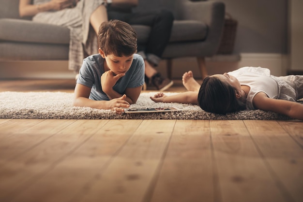 Playtime é tempo de aprendizagem Foto de um adorável irmão e irmã usando um tablet digital em casa com seus pais ao fundo