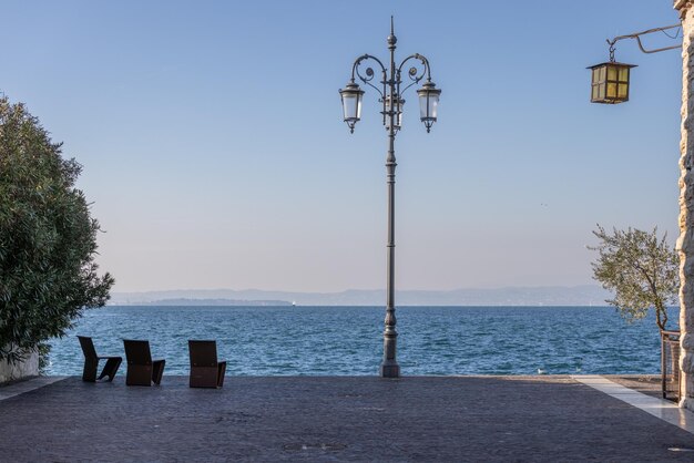 Foto plaza frente al mar de la ciudad de lazise sillas metálicas poste de luz lago de garda vista de italia