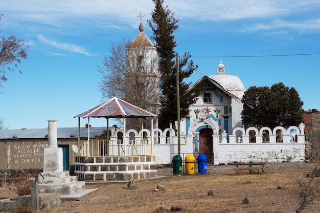 Foto plaza simple con pequeños puestos de música, contenedores de colección selectiva e iglesia católica en el pueblo de jirira en bolivia