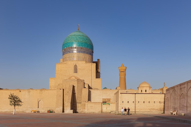 Plaza vacía con antiguas murallas mezquita con gran cúpula colorida y minarete Bukhara Uzbekistán