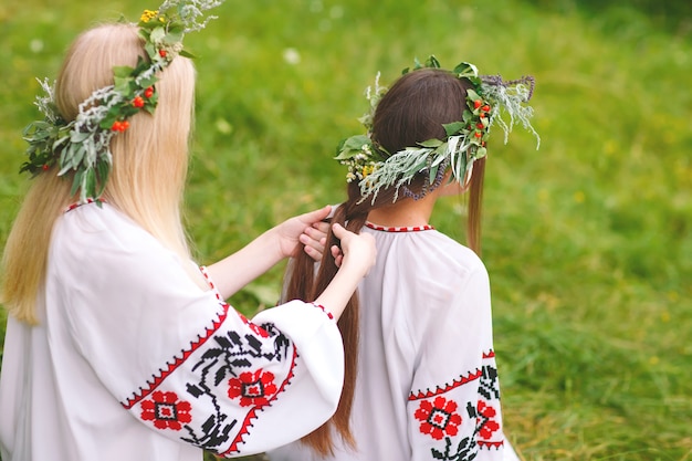 Pleno verano. Dos chicas con ropa eslava tejen trenzas en el cabello