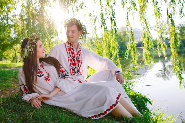 Pleno verano. Joven pareja amorosa en trajes eslavos en la orilla del lago. Fiesta eslava de Ivan Kupala.