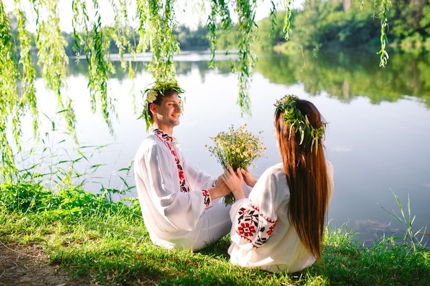 Pleno verano. Joven pareja amorosa en trajes eslavos en la orilla del lago. Fiesta eslava de Ivan Kupala.