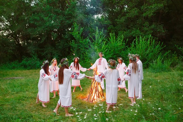 Pleno verano. Los jóvenes en círculo de ropa eslava bailan alrededor de una hoguera en el bosque.