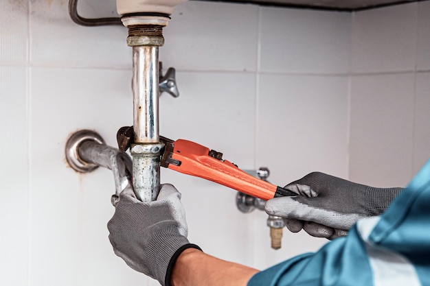 Plomero usando una llave inglesa para reparar la tubería de agua debajo del fregadero