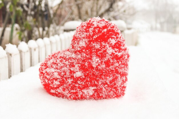 Plüschtierherz, das auf einer Bank vor einem verschneiten Winterhintergrund liegt Valentinstag und Liebeskonzept