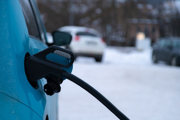 Plugue do carregador inserido no carro elétrico em fundo de inverno com neve